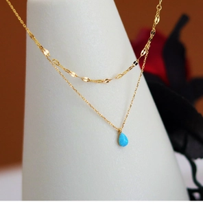 Detail of double-layer gold necklace featuring a light blue teardrop faux opal pendant