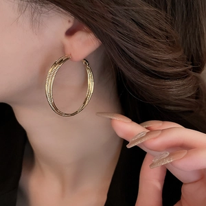 Détail de grandes créoles dorées avec texture tressée portées par un mannequin femme