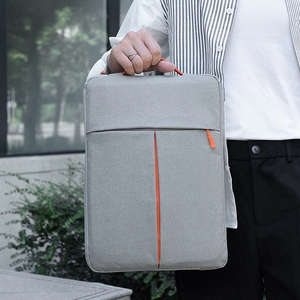 Slim laptop sleeve in light grey with orange zipper held by person in outdoor setting