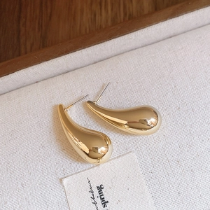 Vue détaillée de boucles d'oreilles dorées en forme de larme sur un fond de tissu texturé