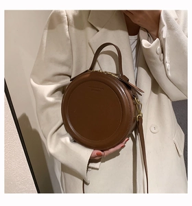 Detail der runden dunkelbraunen Lederhandtasche mit goldenen Beschlägen auf hellem Blazer
