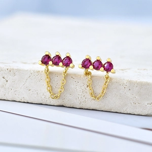 Macro shot of three round-cut red rubies on gold studs with elegant hanging chains