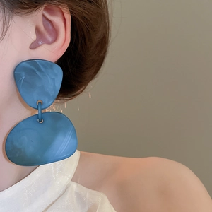 Macro shot of large blue marbled acrylic geometric drop earrings worn by a model