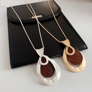 Detail of gold and silver snake chain necklaces with waterdrop pendants on black leather