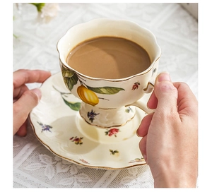 Close-up of hands holding a lemon pattern ceramic coffee cup over a lace tablecloth