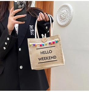 Detail of jute tote bag with colorful pom-poms and 'HELLO WEEKEND' print on natural fabric