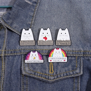 Close-up of five cute cat enamel pins featuring humorous quotes on a denim jacket pocket