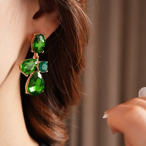 Close-up of vintage teardrop earrings with green faceted gems and gold finish