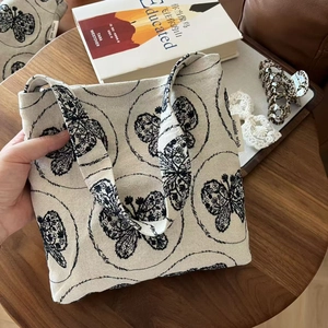 Close-up of beige canvas tote bag with black butterfly embroidery on wooden desk