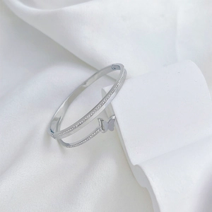 Bracelet manchette papillon argenté avec strass brillants sur fond de soie blanche