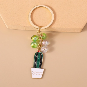 Detail of green beaded cactus keychain with white pot and gold ring on beige background
