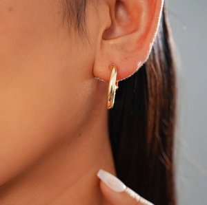 Gros plan de créoles dorées classiques avec finition miroir polie sur l'oreille du modèle