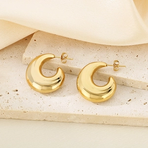 Détail des boucles d'oreilles créoles C en or 18 carats sur un support en pierre texturée