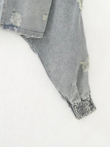 Detail of washed grey denim jacket featuring distressed ripped holes and elastic cuffs