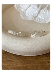 Detail of silver bow and pearl open rings on a lace fabric with soft aesthetic lighting