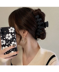 Gros plan sur une pince à cheveux géométrique noire mate fixant une queue de cheval