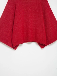 Detailed view of red knit texture and loose hem of an American style poncho sweater
