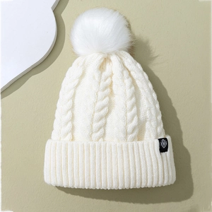 Detailed cable knit pattern on white winter beanie with snowflake patch and pom-pom