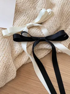 Detail of satin bow hair clips with long ribbons in black and cream on soft fabric