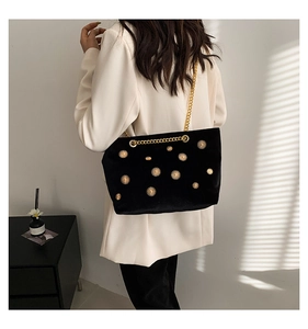 Detail of black velvet tote bag with gold sun rivets and chain strap on a white blazer