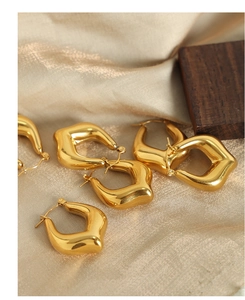 Close-up of thick gold-plated geometric earrings on beige satin with luxury texture
