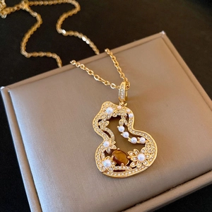 Détail du collier pendentif gourde dorée avec œil de tigre et perles sur boîte à bijoux
