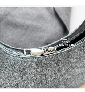 Detailed close-up of the smooth silver metal zipper on a grey textured fabric crescent bag
