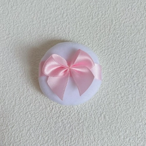 Close-up of a white plush crystal velvet powder puff with a delicate pink satin bow