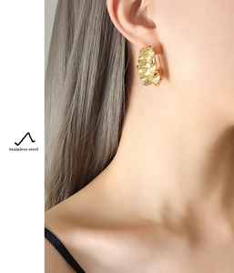 Détail d'un mannequin portant des boucles d'oreilles en acier doré à texture plissée