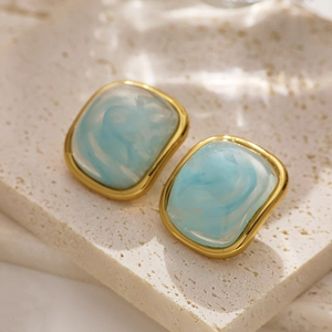 Macro shot of retro square gold earrings featuring blue marbled resin on stone background