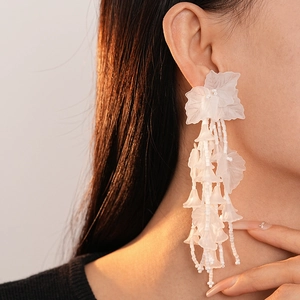 Detail of elegant white acrylic leaf tassel earrings worn on model for a resort style look