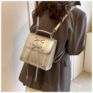 Close-up of a silver metallic backpack with bow detail worn over a dark grey blazer