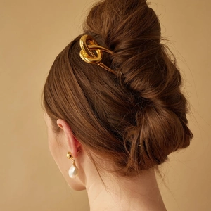 Detail of a 18k gold-plated stainless steel knot hair pin worn by a model in a natural setting