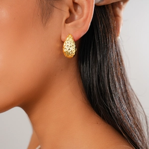 Gros plan d'une boucle d'oreille goutte dorée à texture martelée portée par un modèle