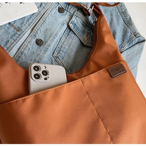 Detail of caramel canvas tote bag placed on denim jacket with fashion label showing