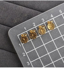 Macro detail of 10mm golden S925 silver round charms with embossed Buddhist relief texture