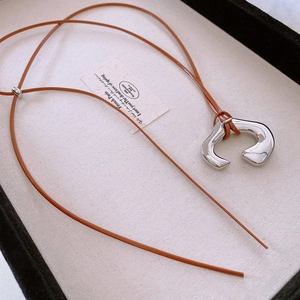 Detail of irregular silver liquid metal pendant on a brown cord necklace displayed on a tray