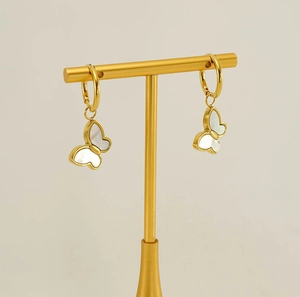 Detail of gold butterfly earrings with white mother-of-pearl wings on a jewelry stand