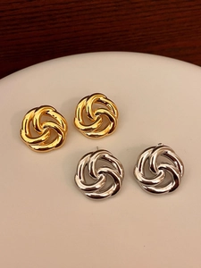 Macro view of knotted flower stud earrings in gold and silver finish on display