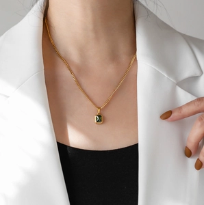 Dettaglio di una collana a catena dorata con ciondolo smeraldo rettangolare su modella