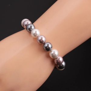 Detail eines mehrfarbigen Muschelperlenarmbands mit weißen, lila und grauen Perlen am Handgelenk