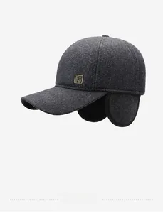 Detail of dark grey wool baseball cap showing earflaps and vintage metal logo plaque