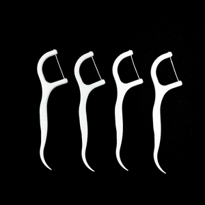 Four white disposable dental floss picks for oral care on a high-contrast black background