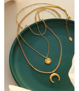 Detail of layered gold necklaces with star and moon charms on a green ceramic plate