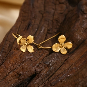 Detailed macro view of gold flower hook earrings on a rustic dark wooden background
