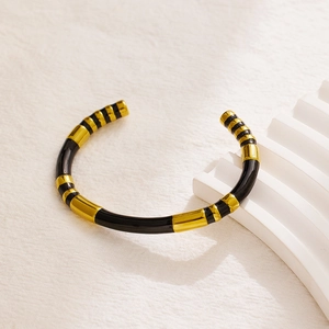 Detail of gold and black enamel striped stainless steel open bangle on white podium