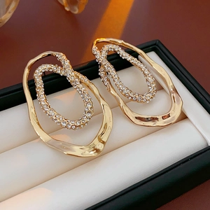 Close-up of gold-plated oval stud earrings featuring shimmering crystals and a dual-ring design