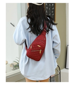 Detail of red quilted oxford chest bag featuring gold zippers and adjustable strap on model
