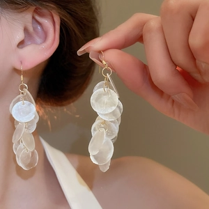 Detail of layered white shell disk drop earrings on model with golden metal accents
