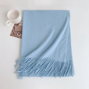 Detail of light blue pashmina scarf with soft fringes on a white minimalist surface